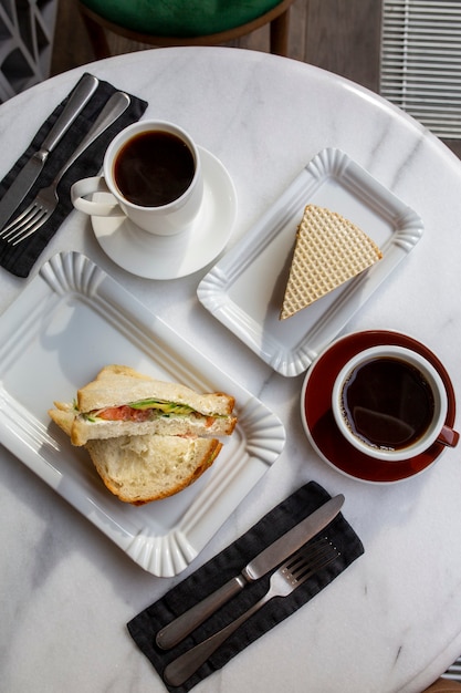 Tasse Kaffee mit Dessert auf dem Marmortisch. Kaffeetag. Frühstück auf weißem Grund. Heißes Getränk mit Kuchen. Draufsicht auf aromatischen Kaffee. Schwarzer Kaffee zum Essen. Frühstück in einem Café. Tag des Essens