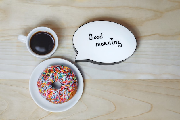 Tasse Kaffee mit einem Donut und einer Platte auf einem Holzbeschaffenheitshintergrund. Konzept zum Thema Guten Morgen.