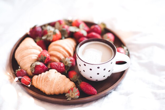 Tasse Kaffee mit Erdbeercroissants auf Tablett in Bettnahaufnahme. Guten Morgen.