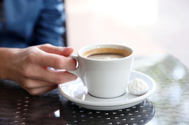 Tasse Kaffee mit Händen und Zephyr auf dem Tisch im Café-Hintergrund