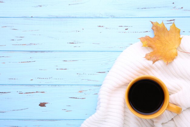 Tasse Kaffee mit Herbstblatt und -strickjacke auf hölzernem Hintergrund