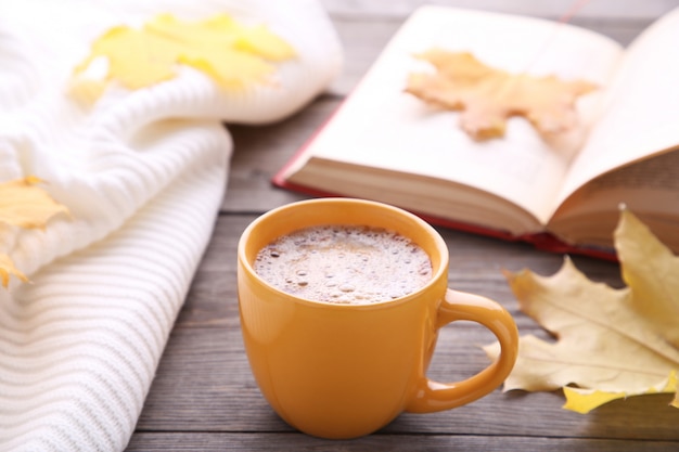 Tasse Kaffee mit Herbstlaub und altem Buch auf hölzernem Hintergrund