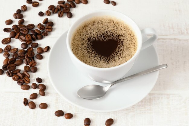 Foto tasse kaffee mit herzmuster und kaffeebohnen auf draufsicht des weißen holztischs