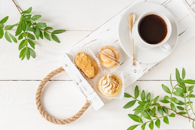 Tasse Kaffee mit Keksen, grünen Blättern, goldenem und weißem Tablett des Weinlöffellöffels auf weißem Tisch. Draufsicht