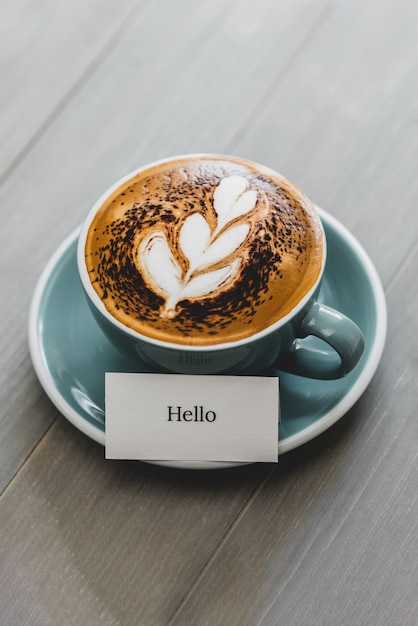 Tasse Kaffee mit Latte Art und Hallo Grußtext auf Holztisch