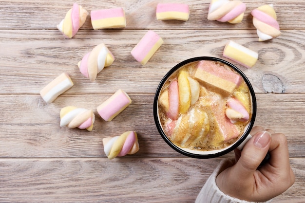 Tasse Kaffee mit Marshmallows in den Händen auf dem Holztisch.