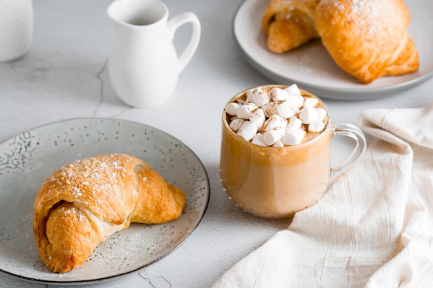 Tasse Kaffee mit Marshmallows und Croissants auf Tellern auf dem Tisch Hausgemachter Frühstückslebensstil