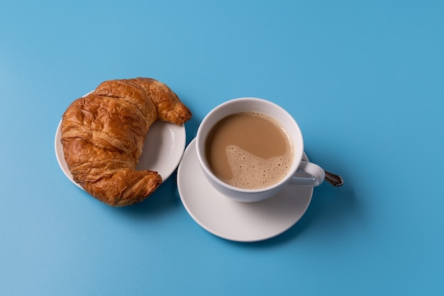 Tasse Kaffee mit Milch auf blauem Hintergrund, mit Croissant, Kopierraum für Text.