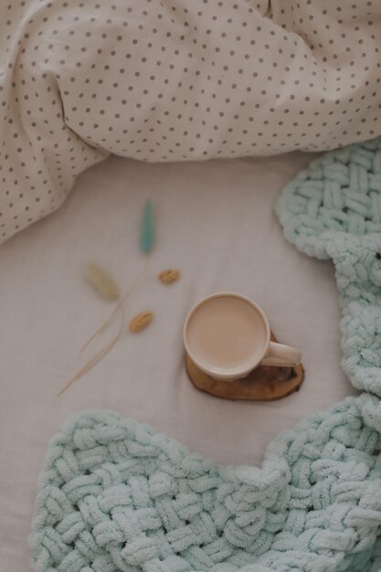 Tasse Kaffee mit Milch auf dem Bett mit weißer Bettwäsche und Decke Morgenkaffee im Bettkonzept