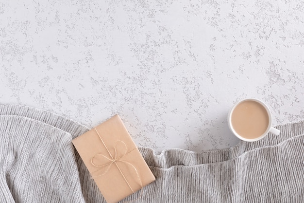 Tasse Kaffee mit Milch auf weißem strukturiertem Hintergrund mit warmem grauem Plaid, Kopienraum. Flachgelegt, Draufsicht