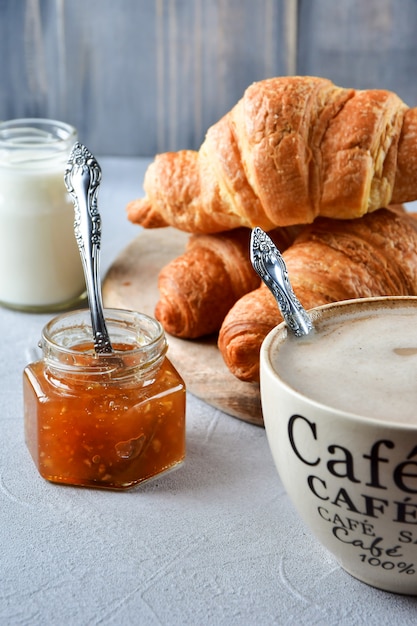 Tasse Kaffee mit Milch und Hörnchen auf einem Holztisch.