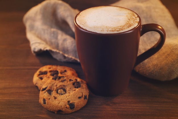 Tasse Kaffee mit Milchschaum und Plätzchen mit Schokoladenkrümeln auf Holzhintergrund