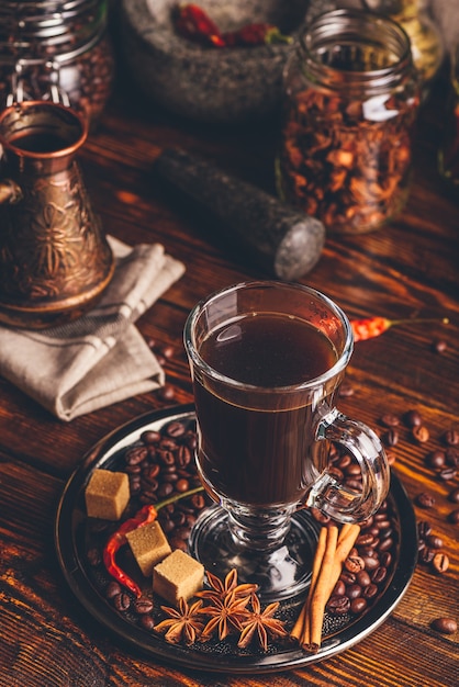 Tasse kaffee mit orientalischen gewürzen auf metalltablett. cezve und einige gläser im hintergrund.