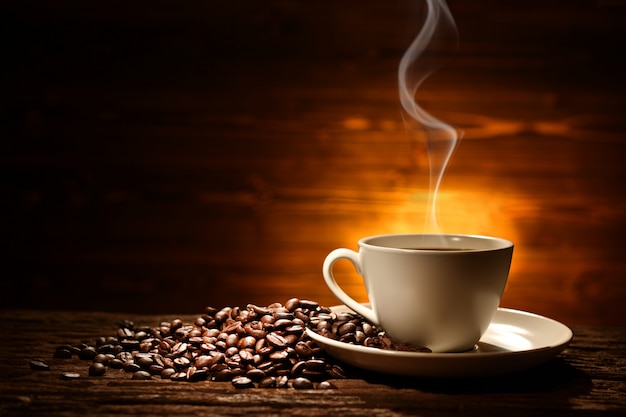 Tasse Kaffee mit Rauch und Kaffeebohnen auf altem Holzhintergrund