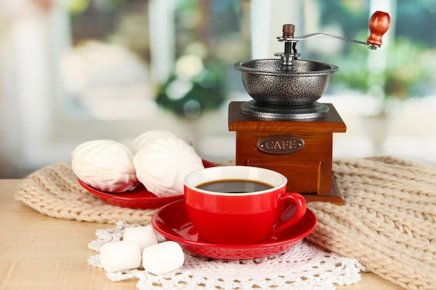 Tasse Kaffee mit Schal und Kaffeemühle auf Tisch im Zimmer