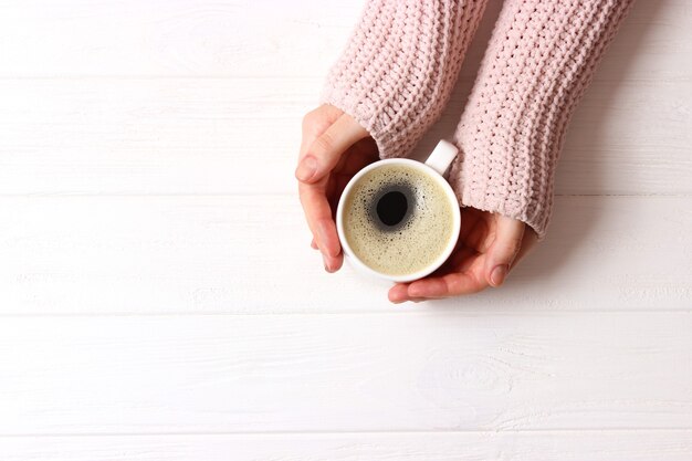 Tasse Kaffee mit Schaum in weiblichen Händen auf Holztisch-Draufsicht