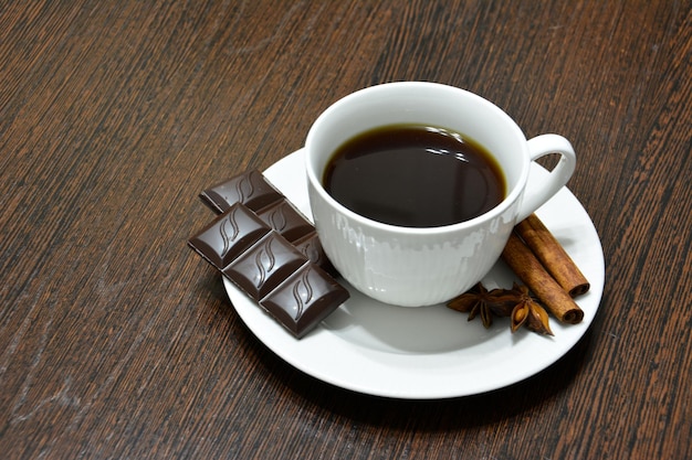 tasse kaffee mit schokolade, zimtbrötchen und badian auf dunklem holzküchentisch