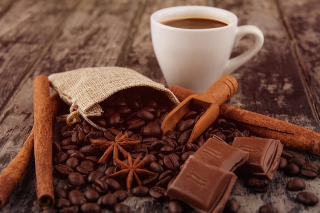 Tasse Kaffee mit Schokoladen-Zimtstangen und Kaffeebohnen auf Holzhintergrund