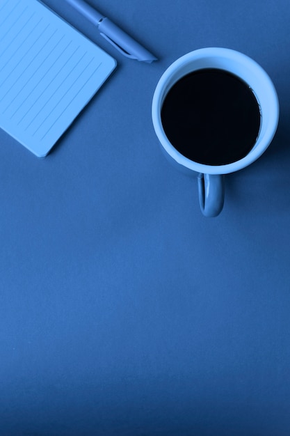 Tasse Kaffee mit Stift und Papier Notizbuch auf blauem Tisch