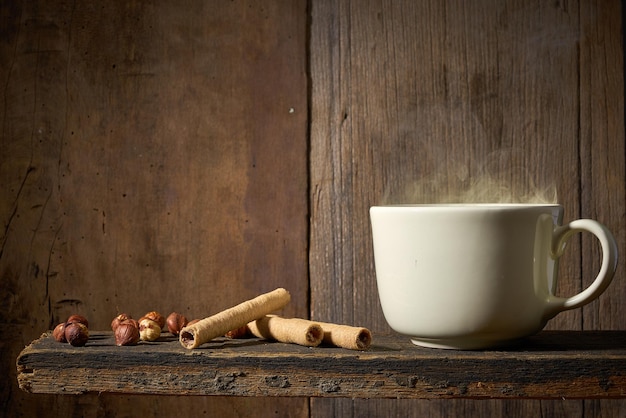 Tasse Kaffee mit Waffelröllchen auf einem Holzregal und Holzhintergrund.