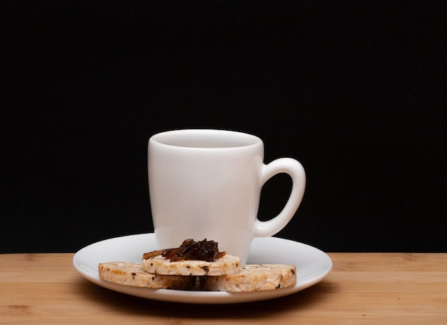 Tasse Kaffee neben einem Reis vegane Kekse mit einem Gelee auf der Oberseite unter dem Holztisch