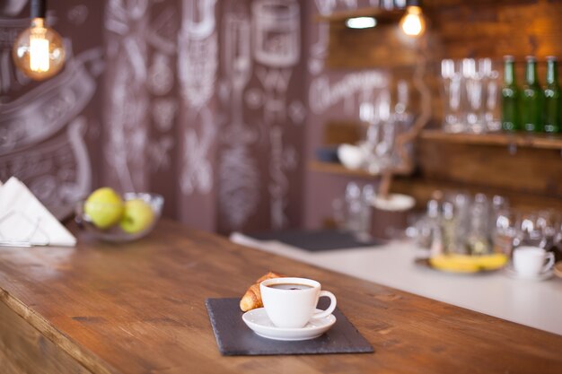 Tasse kaffee neben französischem dessert mit künstlerischer zeichnung im hintergrund. frisch belegtes croissant.