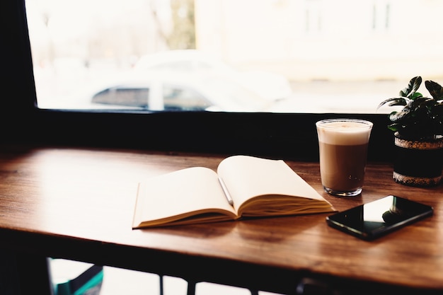 Tasse Kaffee, Notizbuch, Telefon am Tisch im Café. Unscharfer Hintergrund. Hochwertiges Foto