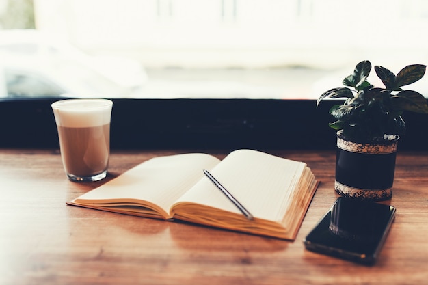 Tasse Kaffee, Notizbuch, Telefon am Tisch im Café