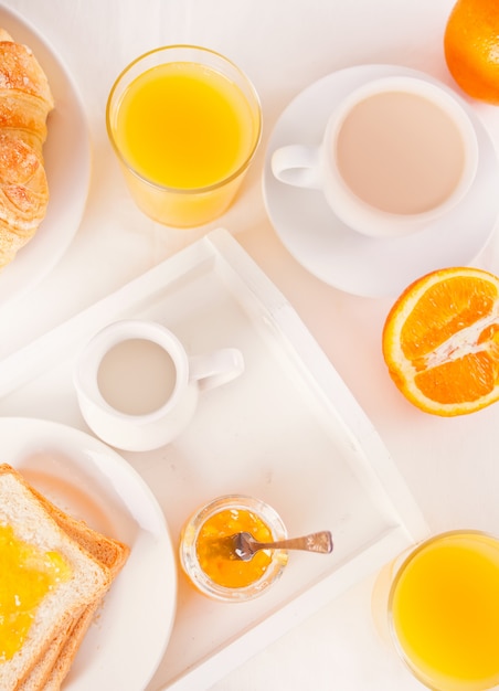 Tasse Kaffee oder Tee, Brot Toast mit Orangenmarmelade, Gläser Orangensaft auf der weißen Oberfläche. Frühstückskonzept. Draufsicht.