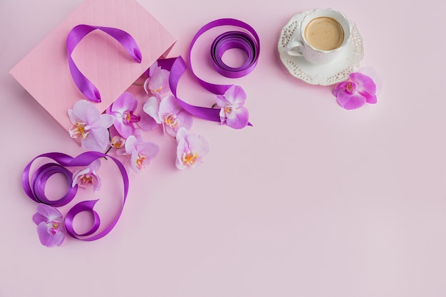 Tasse Kaffee, rosa Geschenktüte mit lila Bändern und rosa Orchideenblumen