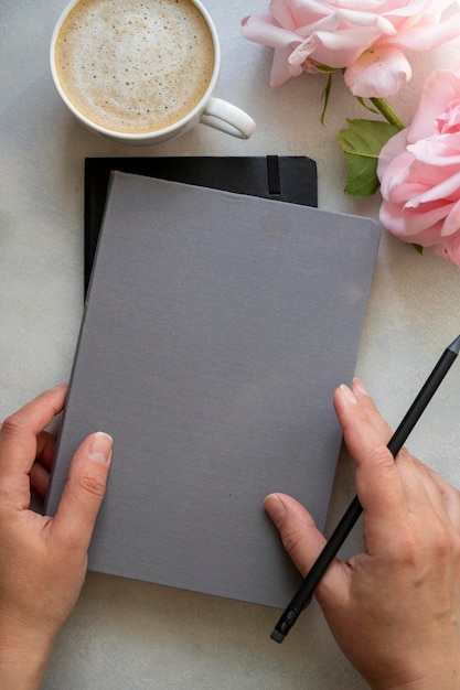 Tasse Kaffee rosa Rosen Blumen und Notebooks mit Frauenhänden auf hellem Hintergrund Tischplatte planen und arbeiten Wohlbefinden entspannen warme Getränke