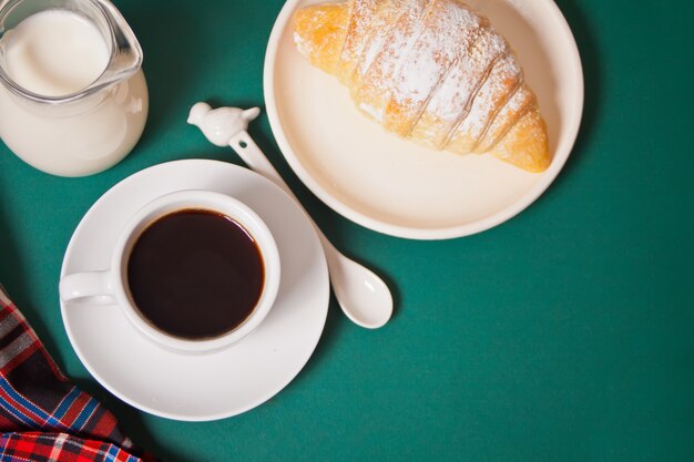 Tasse Kaffee, selbst gemachtes Brötchenhörnchen auf Grün