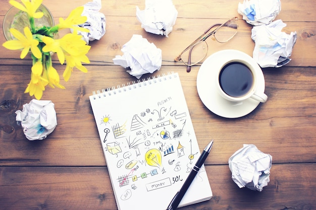 Tasse Kaffee, Stift, Notizblock, Papiere, Gläser und Blumen auf Holztisch