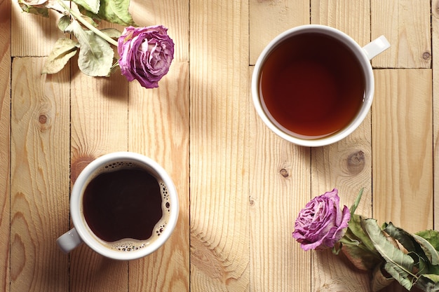 Tasse Kaffee, Tee und zwei getrocknete Rosen auf einem Holztisch