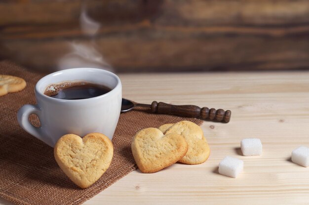Tasse Kaffee und Butterkekse in Form eines Herzens auf Holztisch