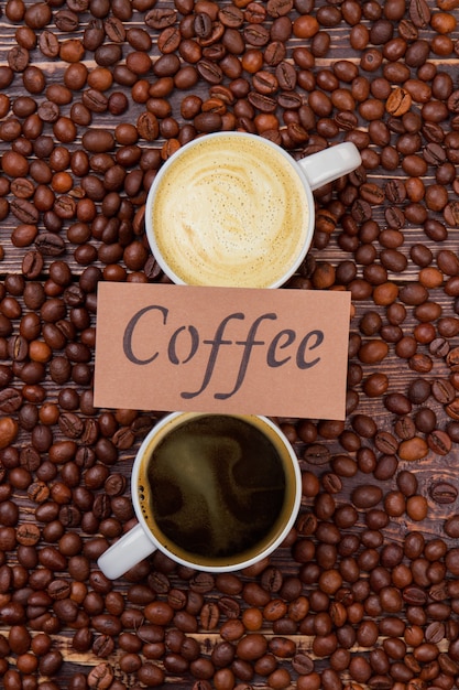 Tasse Kaffee und Cappuccino. Viele Kaffeebohnen auf Holz verstreut.