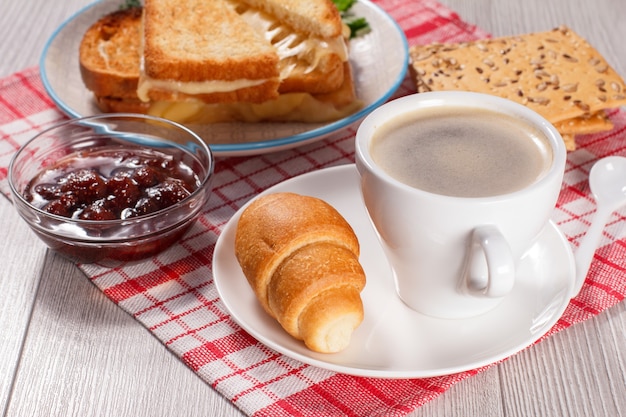 Tasse Kaffee und Croissant auf Untertasse Glasschale mit Erdbeermarmelade Kekse