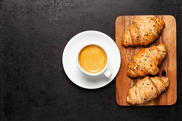 Tasse Kaffee und Croissants, die auf Holzbrett stehen auf altem rustikalem Hintergrund stehen