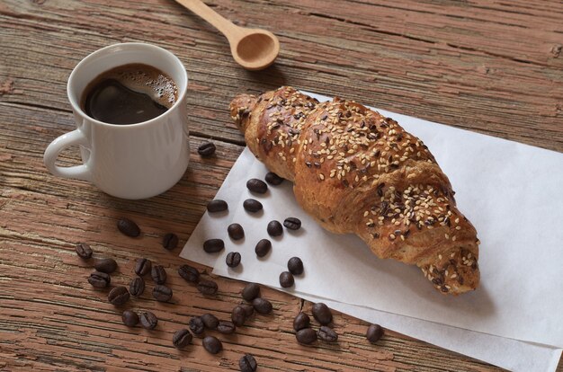 Tasse Kaffee und ein Croissant mit Leinsamen auf einem alten Holztisch