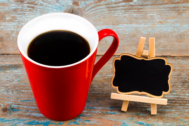 Tasse Kaffee und eine Tafel mit leerem Platz für einen Text auf Holzhintergrund.