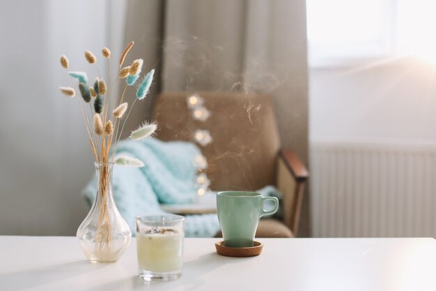 Tasse Kaffee und eine transparente Vase mit getrockneten Blumen am weißen Hintergrund