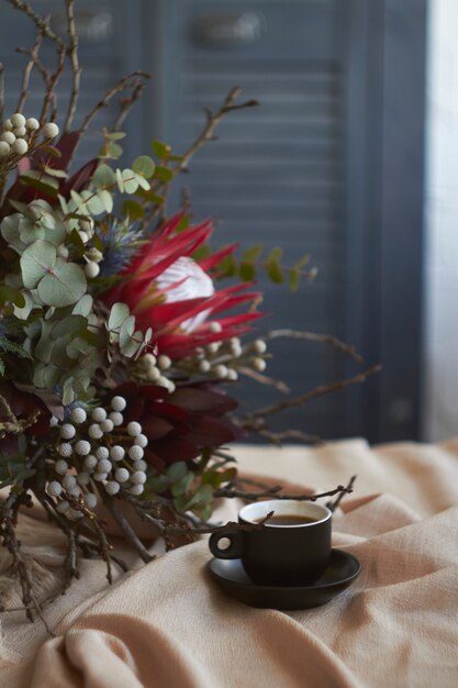 Tasse Kaffee und exotisches Bouquet ohne Verpackung stehen auf Tisch mit beiger Leinentischdecke, Feiertagsmorgenkonzept