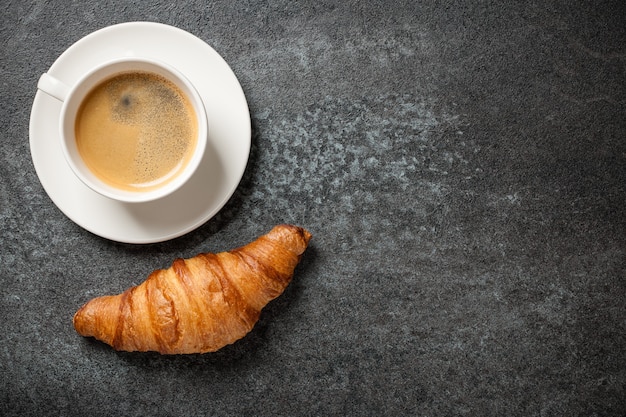 Tasse Kaffee und frisches Croissant auf schwarzem Tisch