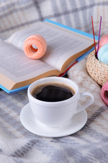 Tasse Kaffee und Garn zum Stricken auf Plaid mit Buch