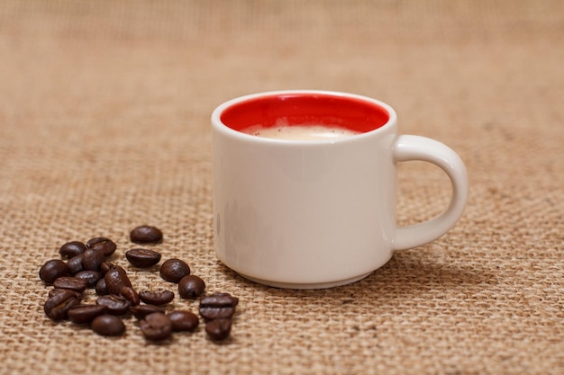 Tasse Kaffee und geröstete Kaffeebohnen auf Sackleinen als Hintergrund.