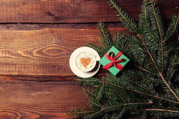 Tasse Kaffee und Herzform neben Geschenkbox und Fichtenzweig auf Holztisch.