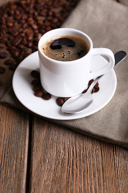 Tasse Kaffee und Kaffeebohnen auf Serviette auf hölzernem Hintergrund