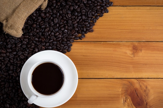 Tasse Kaffee und Kaffeebohnen in einem Sack auf hölzernem Hintergrund.