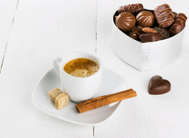 Tasse Kaffee und Kasten Schokoladen auf einem weißen hölzernen Hintergrund
