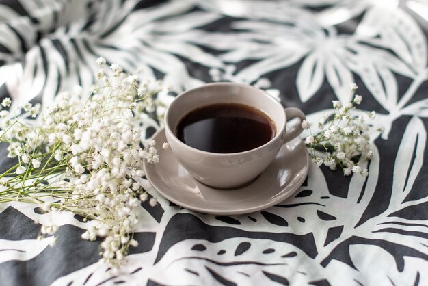 Tasse Kaffee und Kerze auf rustikalem hölzernem Umhüllungsbehälter im gemütlichen Bett mit Decke.